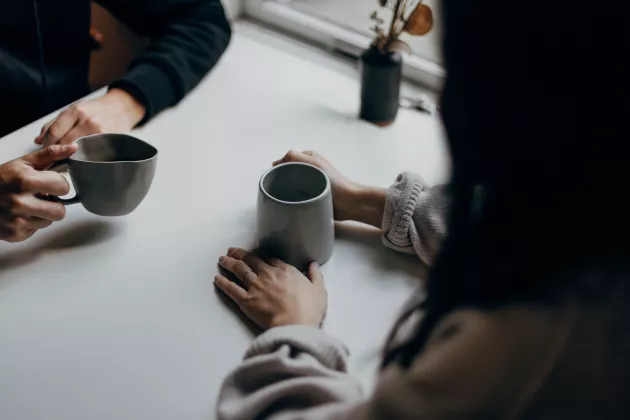 Hands holding two cups of coffee. The people are not visible, but they are having a conversation at a table. Photo.