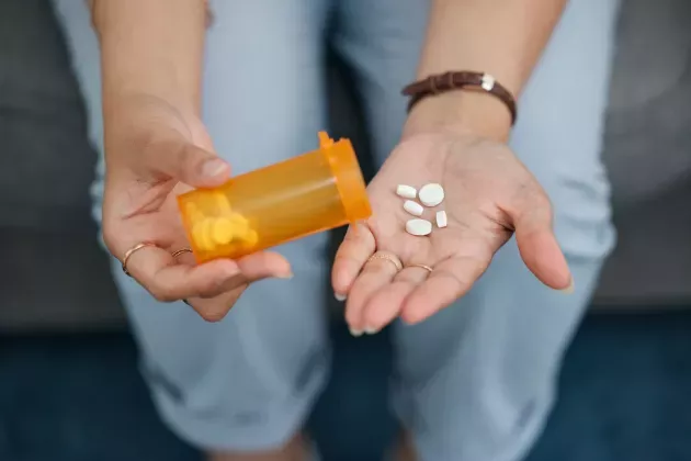 White pills in hand from yellow pill bottle. Photo. 