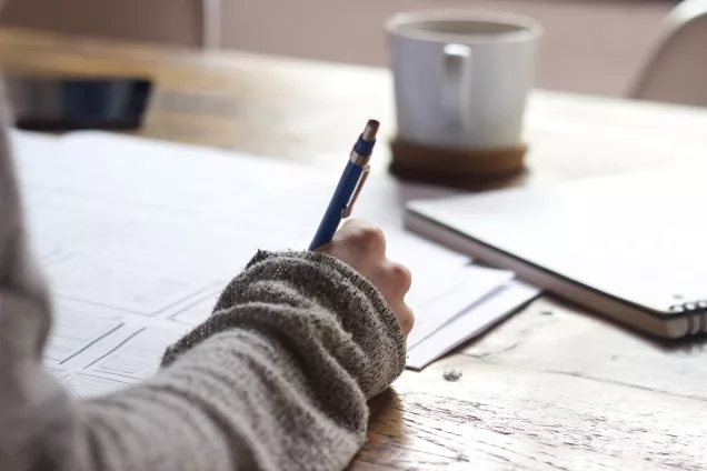 The image shows an arm and a hand writing in a notebook.