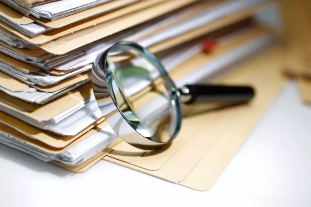 Magnifying glass leaning on stack of paper. Photograph.