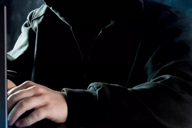 Man klädd i svart hoodie vid dator. Foto.