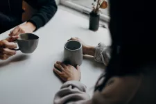 Händer som håller i två koppar kaffe. Man ser inte personerna men de samtalar med varandra vid ett bord. Foto.