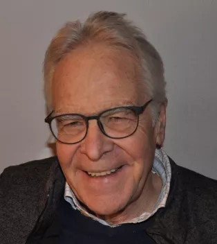 Björn Dahlbäck har glasögon och vitt hår och han ler mot kameran. 